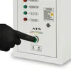A hand wearing a black glove is pressing a green button on a white control panel. Náhled obrázku produktu