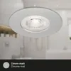 A close-up of a silver recessed ceiling light fixture with a white LED bulb, set against a blurred background of a bathroom. Voir les images du produit
