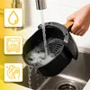 A hand is rinsing an air fryer basket under a faucet in a kitchen sink. There are three informational icons on the left side of the image. Produktbild-Vorschau