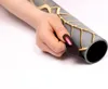 A hand is holding a rolled-up magnetic heater cover with a gold geometric pattern on a gray background. Produktbild-Vorschau