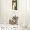 A close-up view of cream-colored curtains with a woven basket filled with flowers placed on a fluffy rug in front of a window. Produktbild-Vorschau