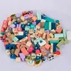 A collection of wooden building blocks and toy vehicles arranged in a circular pattern on a light gray background. Náhled obrázku produktu