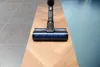 A vacuum cleaner head is shown on a floor that transitions from tiles to wood to carpet. Náhľad obrázku produktu