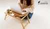 A person is sitting on a white rug, using a laptop on a wooden lap desk. Podgląd zdjęcia produktu