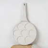 A cream-colored pancake pan with seven circular molds is shown against a textured white and light gray background. Podgląd zdjęcia produktu