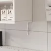 A close-up view of a white bathroom cabinet mounted on a tiled wall, with a shelf bracket visible. Náhled obrázku produktu