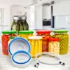 A collection of glass jars filled with preserved food items and a vacuum sealing accessory set, arranged on a wooden surface with a blurred kitchen background. Podgląd zdjęcia produktu