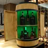 A wooden barrel-shaped cabinet with shelves and bottles inside, illuminated by green LED lights. Produktbild-Vorschau
