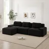 A black modular L-shaped sofa with an ottoman is placed on a light beige rug in a well-lit living room. Two framed abstract art pieces hang on the wall behind the sofa, and a large window with white trim is visible to the left. Produktbild-Vorschau