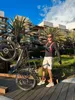 A man is holding an e-bike in front of a building with palm trees. Anteprima dell’immagine prodotto