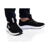 A person wearing black Under Armour sneakers and dark pants, shown from the knees down. Produktbild-Vorschau