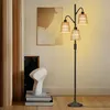 A floor lamp with three rattan shades is placed in a room next to a piece of abstract art and a sculpture. Náhľad obrázku produktu