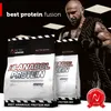 A muscular man holding a rope is featured in the background, with two bags of protein powder in the foreground. Produktbild-Vorschau