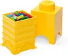 A yellow LEGO storage brick and a stack of yellow storage containers filled with LEGO bricks. Produktbild-Vorschau