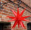 A red star ornament hangs from a black metal bracket attached to a brick wall. Produktbild-Vorschau