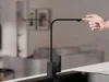 A hand is shown interacting with a black kitchen faucet in a modern kitchen setting. Produktbild-Vorschau
