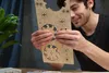 A man is holding and examining a wooden 3D puzzle kit. Produktbild-Vorschau