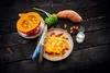 A prepared meal with ingredients arranged around it on a dark wooden surface. Produktbild-Vorschau