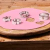 Cookie cutters are being used to cut shapes out of pink fondant on a wooden board. Produktbild-Vorschau