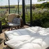 A cozy seating area and a bed are set up inside a greenhouse with a view of a field. Produktbild-Vorschau