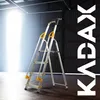 A silver and yellow stepladder is shown in a warehouse-like setting with bright light coming from an opening. Podgląd zdjęcia produktu