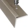A close-up view of a bronze-colored stair nosing profile with a drill bit creating a hole in it. Podgląd zdjęcia produktu