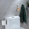 A toilet paper holder attached to the side of a toilet tank, with a towel and bath brushes hanging on hooks on the wall. Produktbild-Vorschau