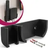 A black wall mount designed to hold a TV remote and a small media box, shown with screws and wall plugs. Produktbild-Vorschau