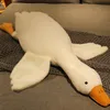 A large white goose plush toy lying on a gray blanket on a sofa. Produktbild-Vorschau