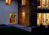 Exterior view of a modern house at dusk, showing a wooden-clad wall with an outdoor light fixture and a patio area. Produktbild-Vorschau