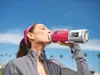 A woman drinking a smoothie from a portable blender outdoors. Podgląd zdjęcia produktu
