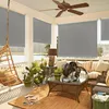 A covered porch or balcony furnished with outdoor seating, plants, and a hanging chair, with gray roller shades drawn. Náhled obrázku produktu