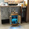 A wine barrel cabinet with illuminated shelves displaying bottles, placed on a floor in front of a bar. Produktbild-Vorschau