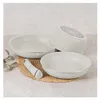 A set of three cream-colored bowls with silver rims, one of which is upside down, and a small white kitchen utensil on a woven mat. Produktbild-Vorschau