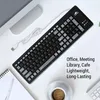 A black USB keyboard is shown on a white desk next to a notebook and a cup of coffee. Produktbild-Vorschau
