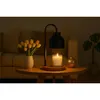 A candle warmer lamp sits on a wooden table next to a vase of yellow tulips and a small golden vase. A couch is visible in the background. Náhled obrázku produktu