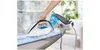 A hand is using an iron on an ironing board, with another iron in the background. Produktbild-Vorschau