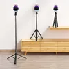 Three black selfie sticks with phones attached are displayed in a room with a white wall and wooden furniture. Náhled obrázku produktu