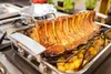 A roasted rack of pork with potatoes in a roasting pan on a stovetop. Produktbild-Vorschau