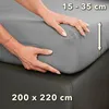 Hands adjusting a grey fitted sheet on a mattress. Produktbild-Vorschau