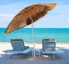 Two lounge chairs and a straw umbrella on a sandy beach with the ocean in the background. Produktbild-Vorschau