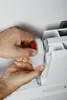 A person's hands are shown adjusting a red knob on a white device attached to a radiator. Náhled obrázku produktu
