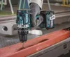 A person wearing gloves is using a Makita cordless drill to drill into a metal beam. Produktbild-Vorschau