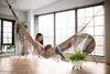 A woman is reading a book in a hammock in a bright, airy room with large windows. Náhled obrázku produktu