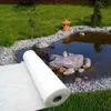 A roll of white drainage fleece is placed on green grass next to a pond with decorative stones and a small pagoda. Produktbild-Vorschau