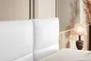 A close-up view of a white upholstered headboard and a bedside lamp. Produktbild-Vorschau