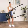 A woman is holding a folded stepper machine in a room with plants and furniture. Voir les images du produit