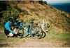 A person is working on a bicycle on a scenic hillside overlooking the ocean. Podgląd zdjęcia produktu