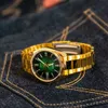 A gold watch with a green dial rests on dark blue denim fabric with visible stitching. Voir les images du produit