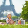 A young girl is having a picnic with a picnic basket and a doll in front of the Eiffel Tower. Produktbild-Vorschau